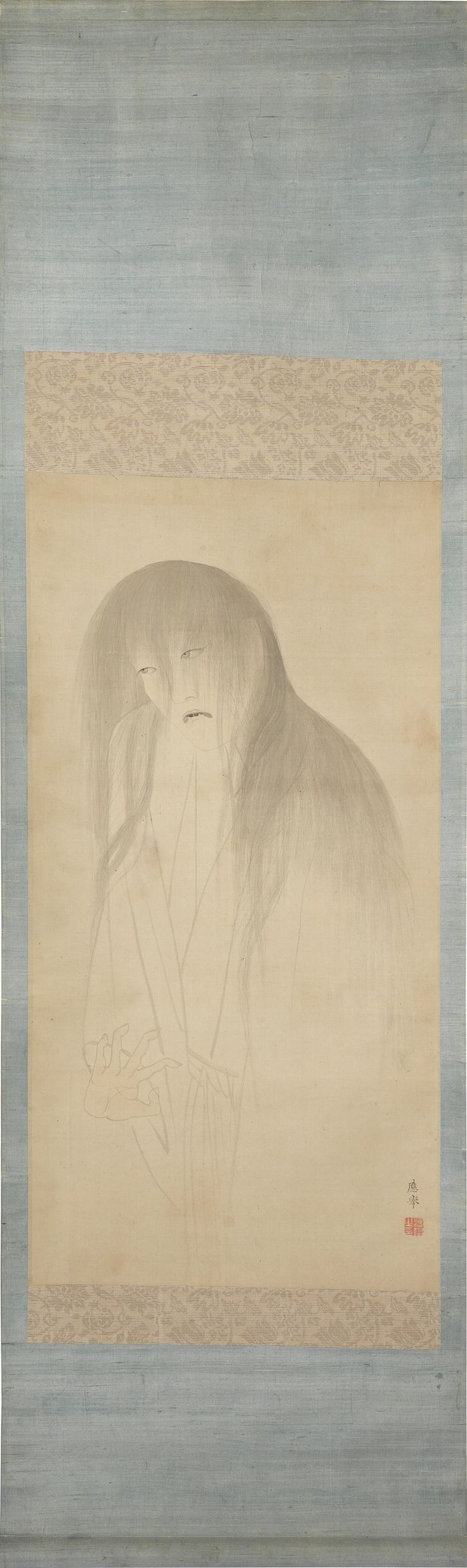 The Ghost of Oyuki mounted as a hanging scroll in pale blue silk: a ghostly woman with long unbound hair, a grimacing mouth and a limp, curled hand, her white robe fading into nothing below the waist.